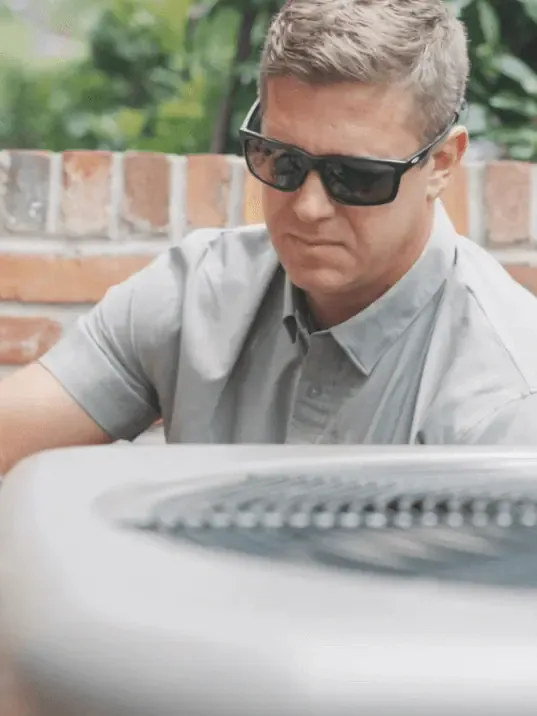 A professional technician from a leading HVAC company in Tallahassee FL performing a detailed inspection of an outdoor air conditioning unit.